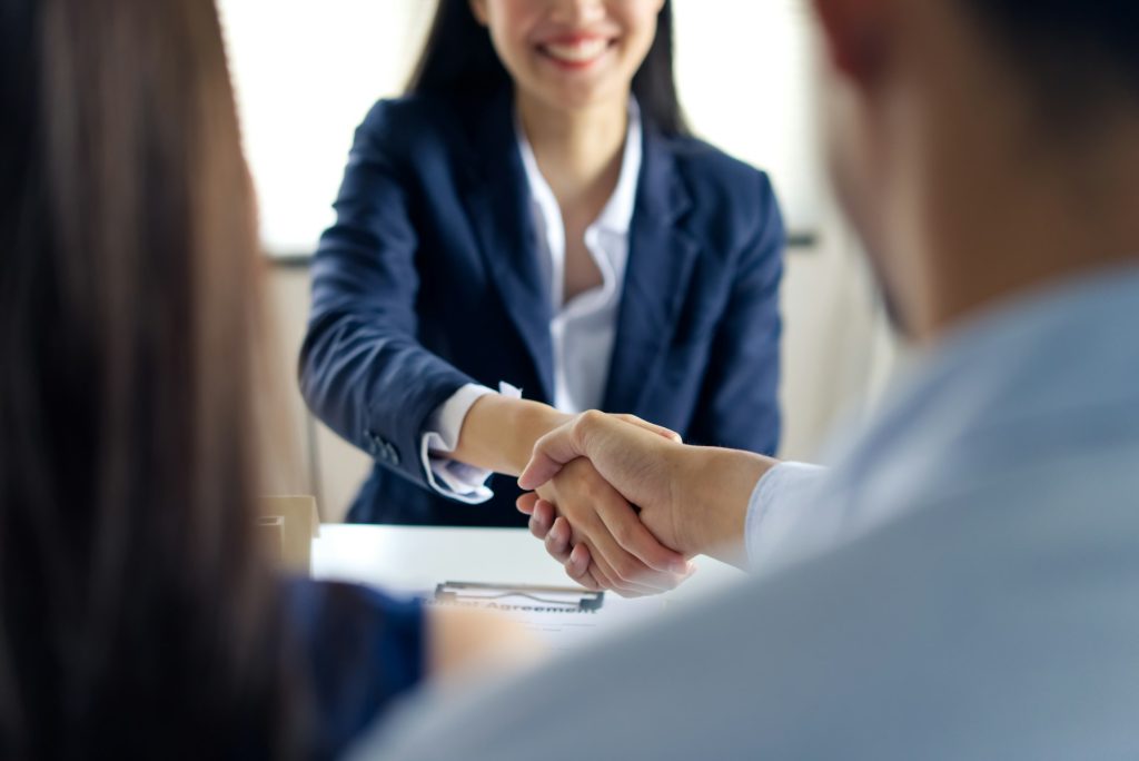 Handshake between Asian couple and young agency girl sitting opposite after successful negotiation.